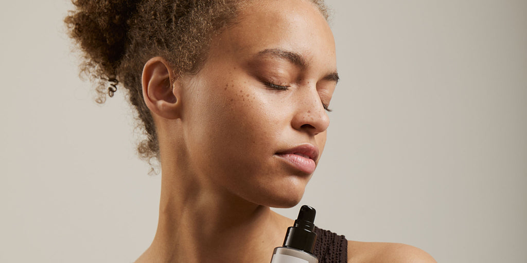 Woman with closed eyes holding skincare product, peaceful expression